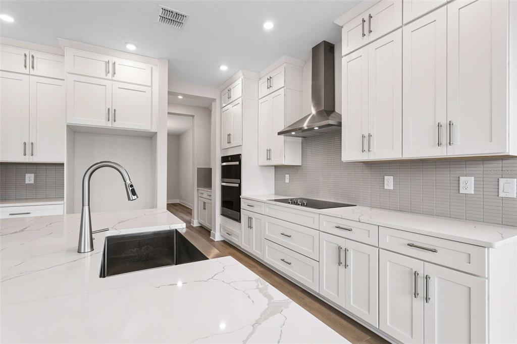 A modern kitchen features white cabinetry, quartz countertops, a stainless steel range hood, and an island — 432 43RD AVENUE NE, ST PETERSBURG, FL