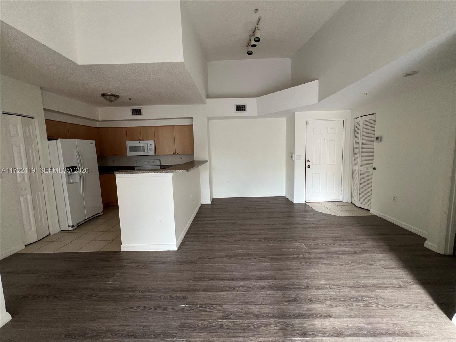 An open-concept kitchen and living area features wood-look flooring, white walls, and a breakfast bar — 2360 E Preserve Way # 305, Miramar FL 33025, MIRAMAR, FL