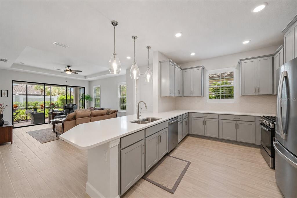A modern kitchen with gray cabinets, white countertops, and a breakfast bar overlooks a living area — 6066 MESA GLEN, BRADENTON, FL