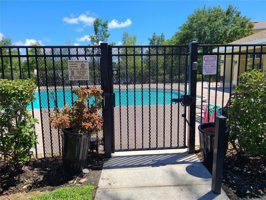 A black metal gate provides access to a swimming pool area with surveillance signage — 7365 BLACK WALNUT WAY, LAKEWOOD RANCH, FL