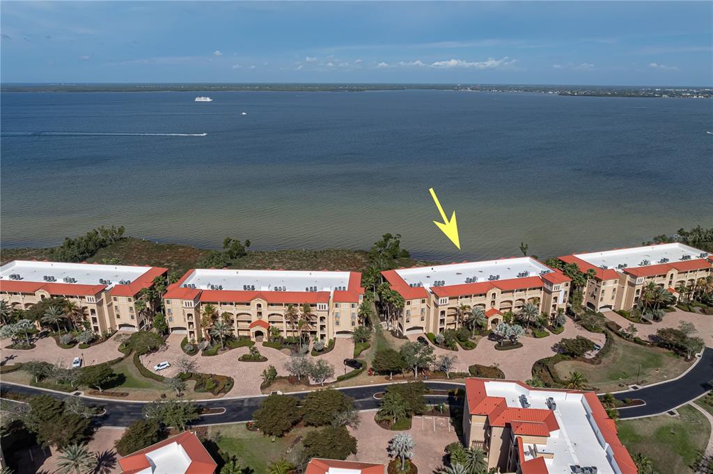 An aerial view shows several multi-story apartment buildings with red roofs near a large body of water — 87 VIVANTE BOULEVARD UNIT 8742, PUNTA GORDA, FL
