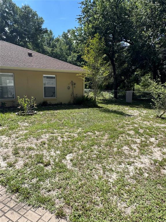 A tan house exterior with two windows sits next to a grassy, sandy backyard — 14431 SE 36TH COURT, SUMMERFIELD, FL