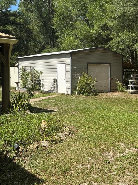 A detached metal garage with a white side door and a roll-up door sits outdoors — 14431 SE 36TH COURT, SUMMERFIELD, FL