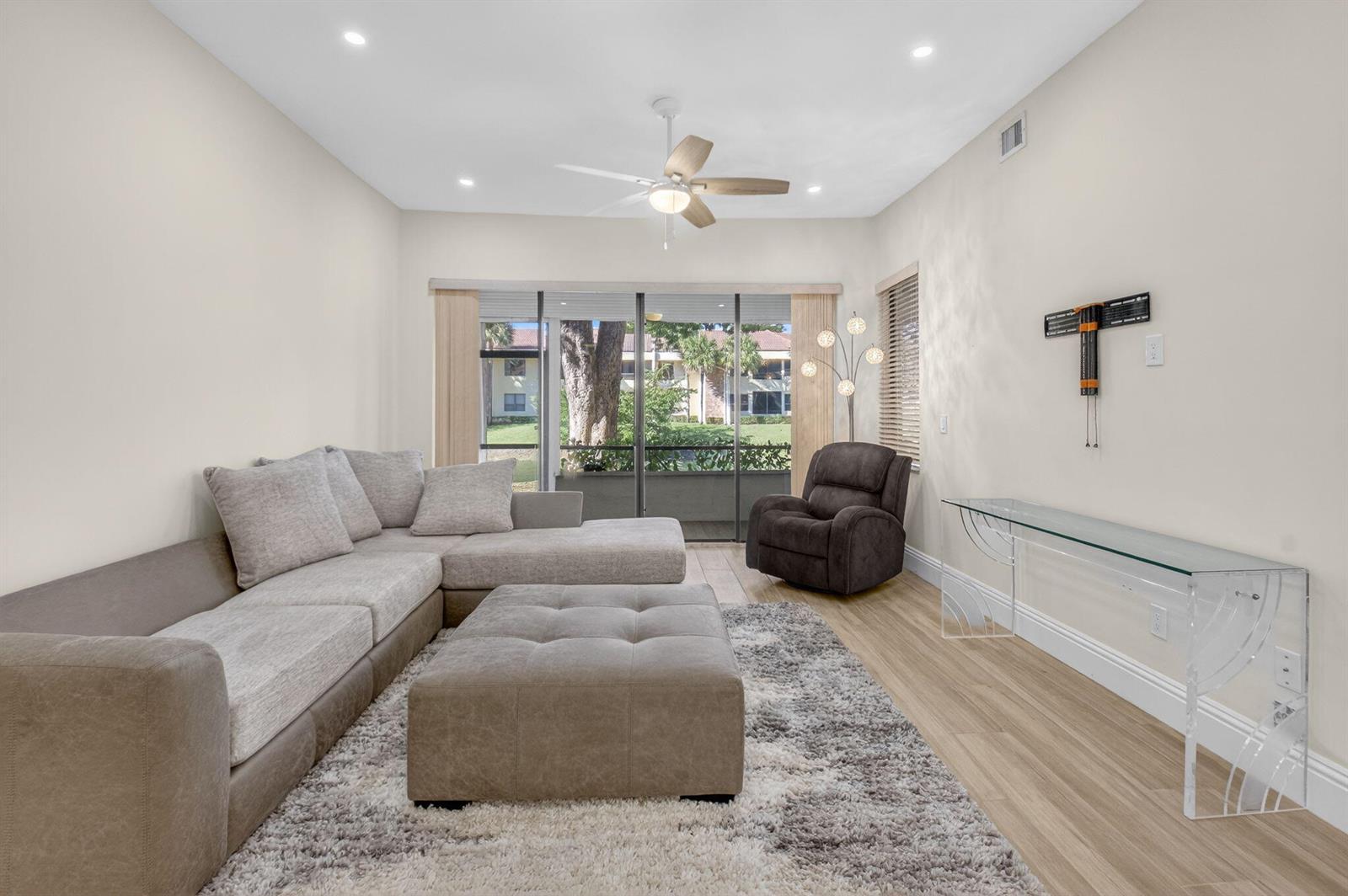 A living room features a sectional sofa, a large ottoman, and a glass console table — 7484 La Paz Boulevard # 103, Boca Raton FL 33433, BOCA RATON, FL