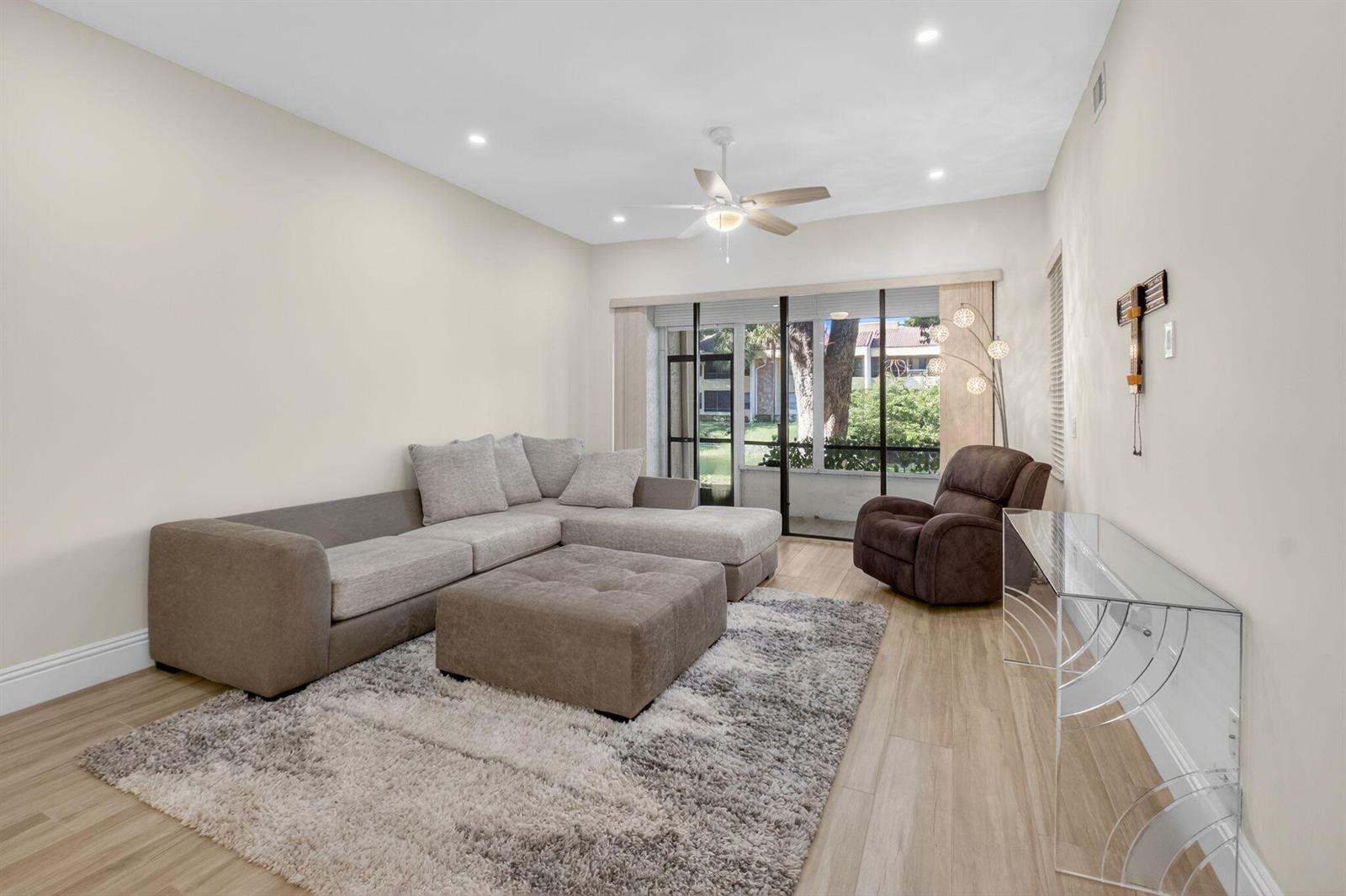 A living room features a sectional sofa, a brown recliner, and a glass console table — 7484 La Paz Boulevard # 103, Boca Raton FL 33433, BOCA RATON, FL