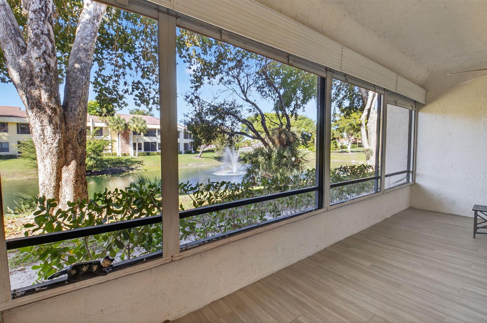 A screened-in porch with wood-look tile flooring overlooks a pond with a fountain — 7484 La Paz Boulevard # 103, Boca Raton FL 33433, BOCA RATON, FL