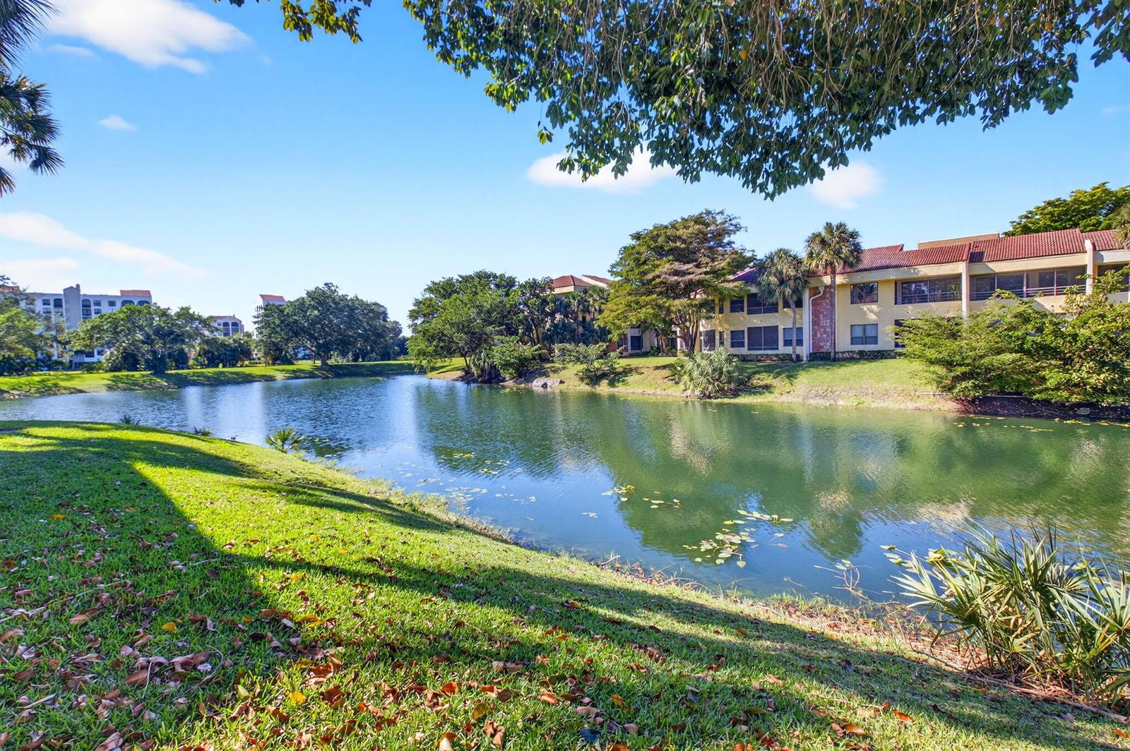 A grassy lawn slopes down to a pond in front of multi-story apartment buildings — 7484 La Paz Boulevard # 103, Boca Raton FL 33433, BOCA RATON, FL