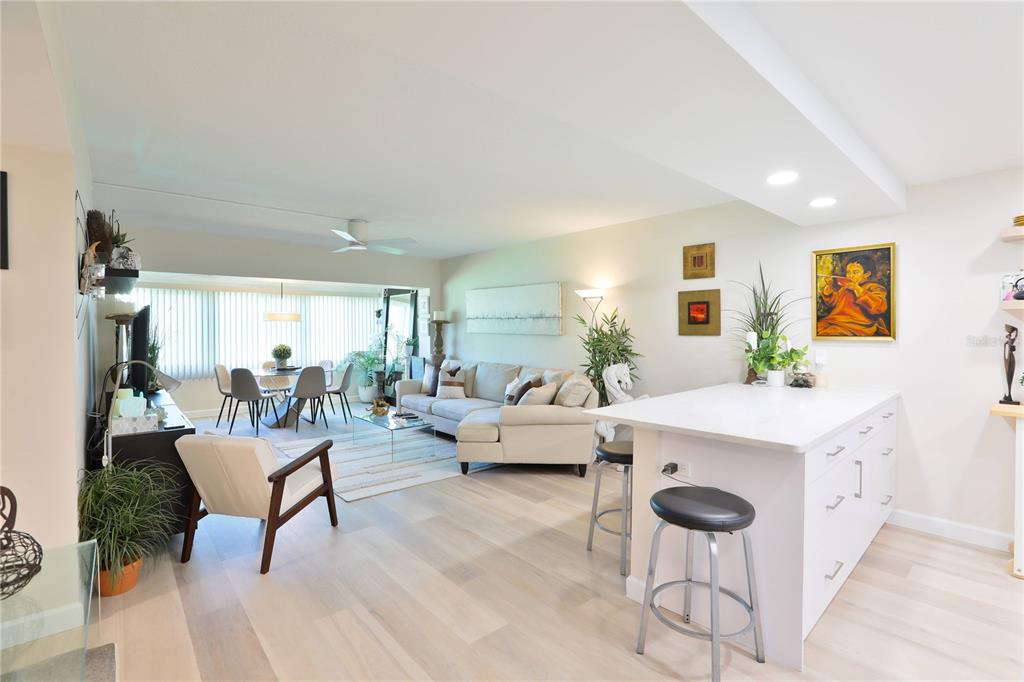 An open-concept living and dining area features light wood floors, a kitchen island, and seating — 4600 98TH WAY N UNIT 209, SEMINOLE, FL
