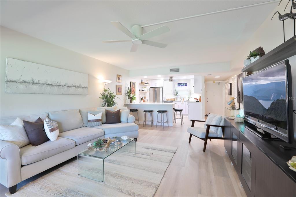 A living room with a sectional sofa, glass coffee table, and an open kitchen beyond — 4600 98TH WAY N UNIT 209, SEMINOLE, FL