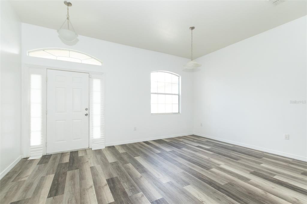 An empty room with white walls, wood-look flooring, a front door, and two pendant lights — 3858 SW 161ST STREET, OCALA, FL