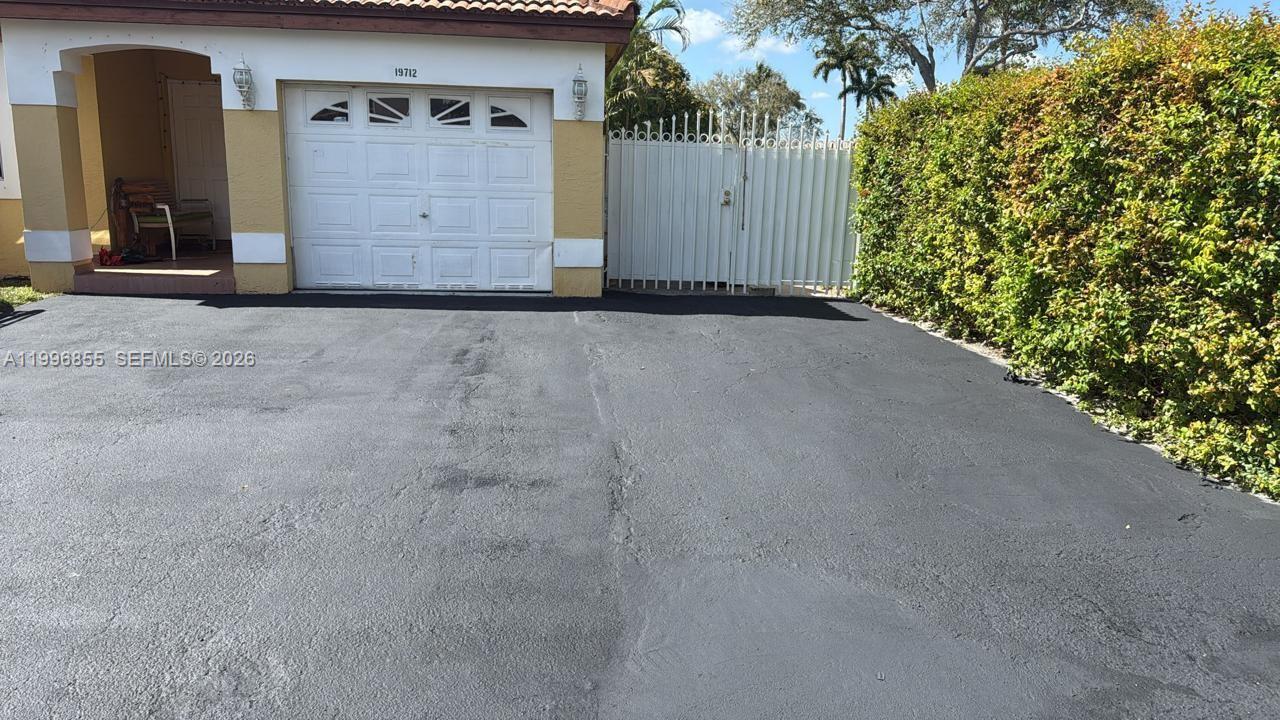 A single-story house exterior features a garage, a paved driveway, and a white metal gate — 19712 NW 82nd Pl, Hialeah FL 33015, HIALEAH, FL