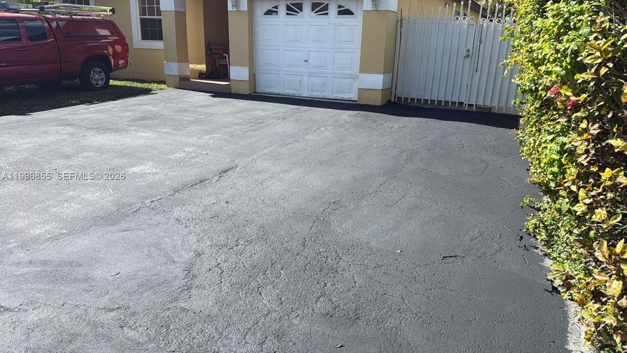 A paved driveway leads to a house with a garage and a white metal gate — 19712 NW 82nd Pl, Hialeah FL 33015, HIALEAH, FL