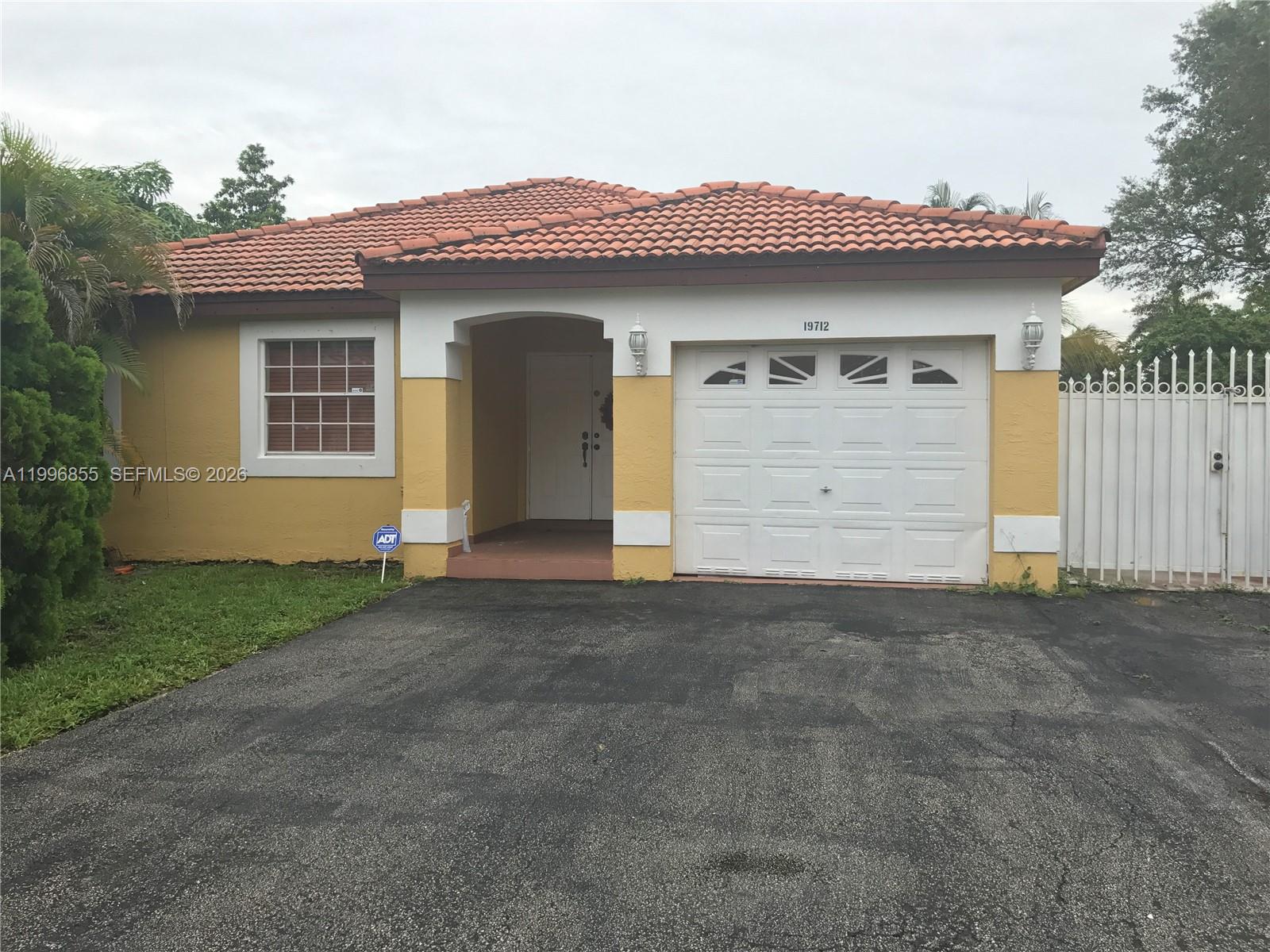 A single-story yellow house features a tiled roof, a white garage door, and a driveway — 19712 NW 82nd Pl, Hialeah FL 33015, HIALEAH, FL
