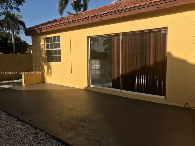 A yellow house exterior features a concrete patio and a large sliding glass door — 19712 NW 82nd Pl, Hialeah FL 33015, HIALEAH, FL