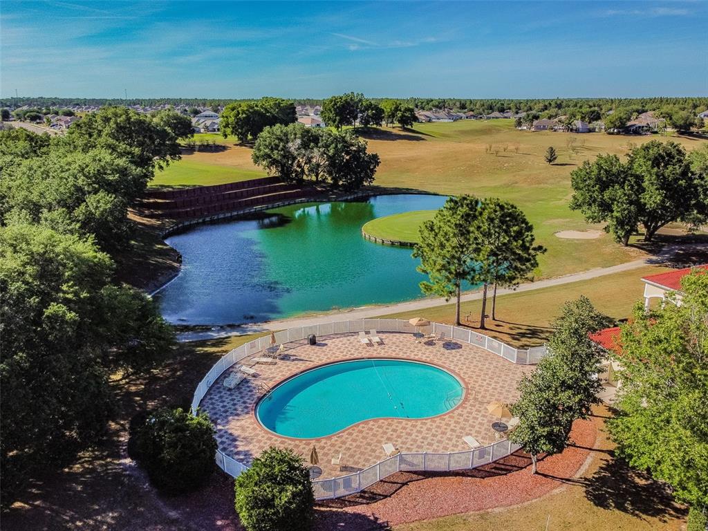 An aerial view shows a kidney-shaped swimming pool next to a pond and golf course — 30821 WATER LILY DRIVE, BROOKSVILLE, FL
