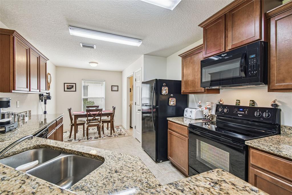 A kitchen with granite countertops, wooden cabinets, and black appliances opens to a dining area — 30821 WATER LILY DRIVE, BROOKSVILLE, FL
