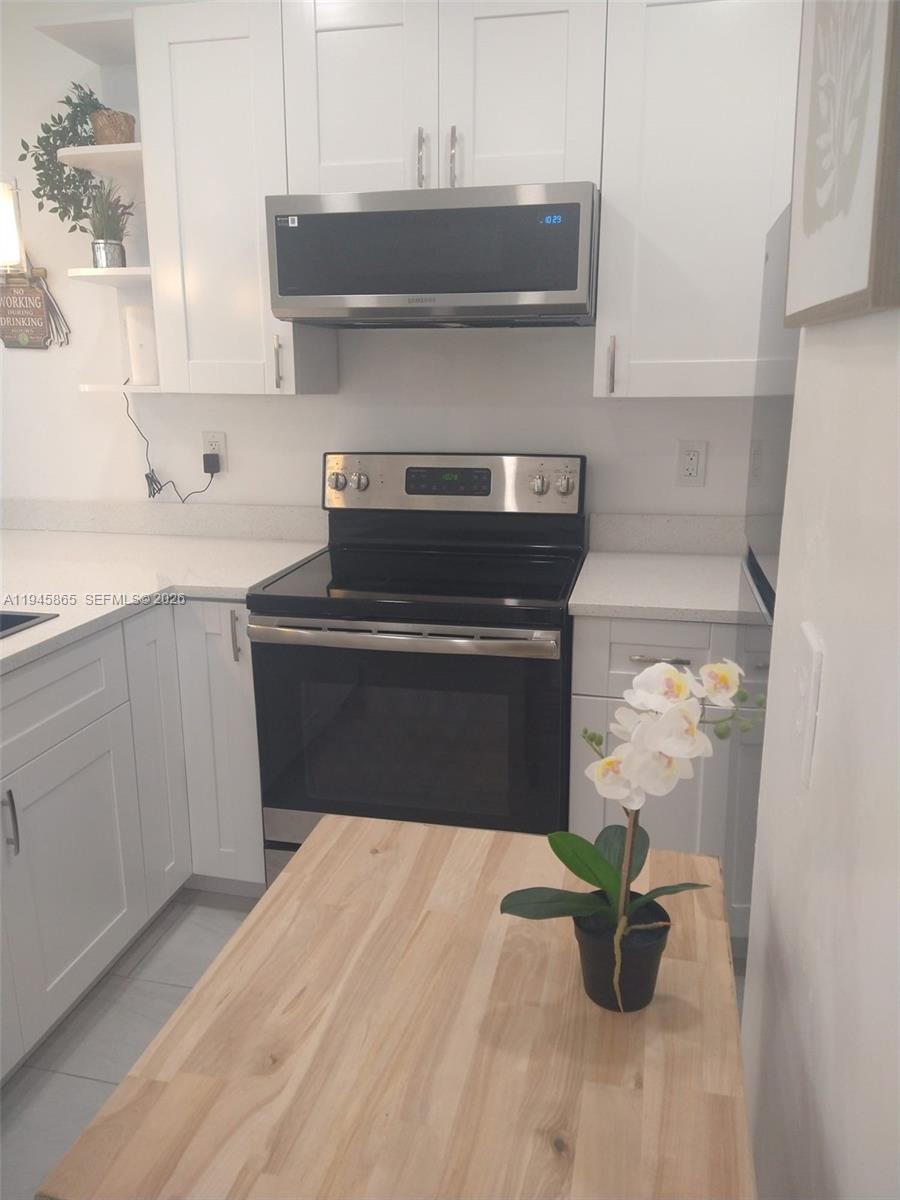 A kitchen features white cabinetry, stainless steel appliances, and a wooden island with an orchid — 600 Layne Blvd # 122, Hallandale Beach FL 33009, HALLANDALE BEACH, FL