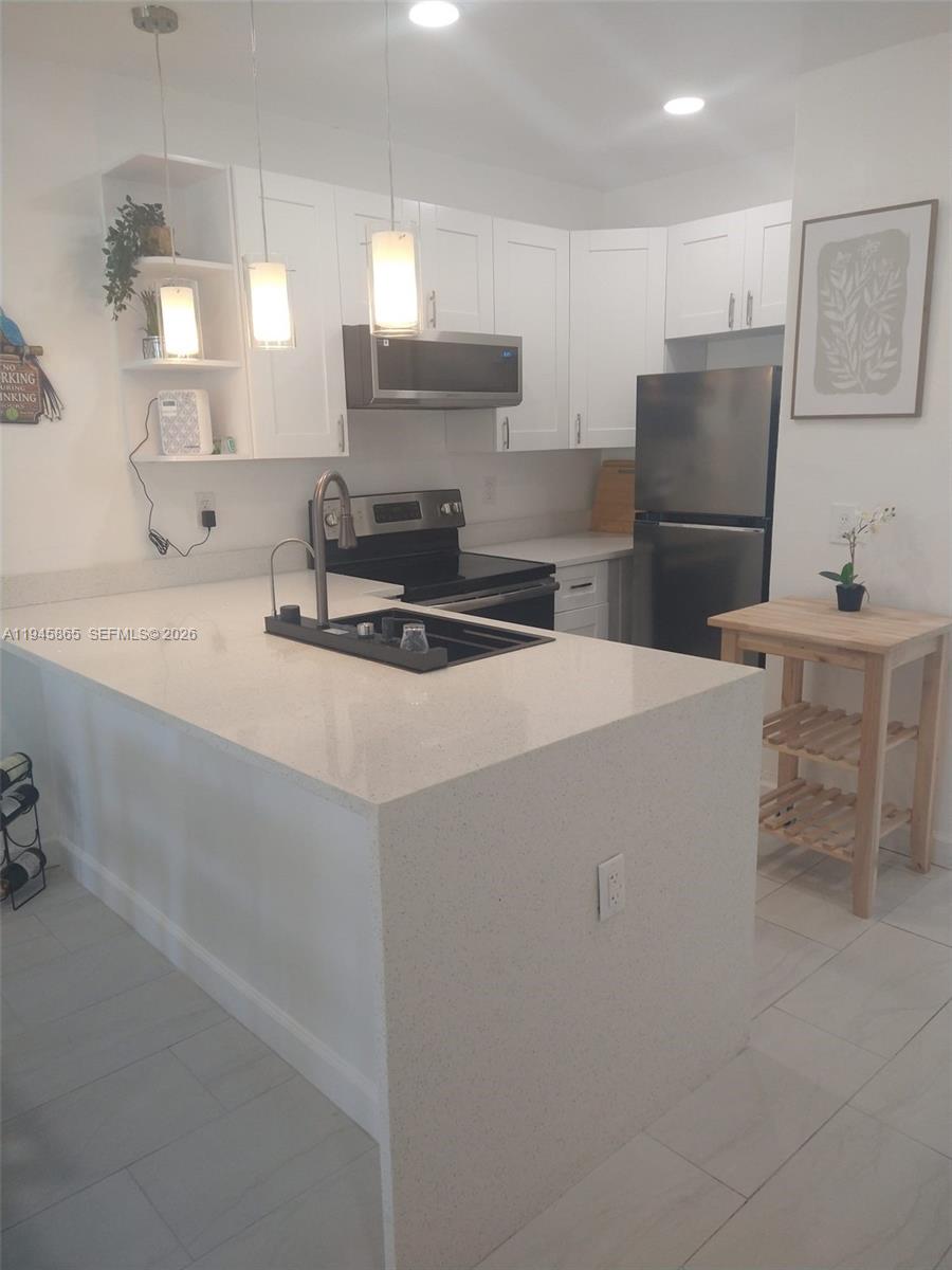 A kitchen features white cabinets, stainless steel appliances, and a white quartz countertop island — 600 Layne Blvd # 122, Hallandale Beach FL 33009, HALLANDALE BEACH, FL