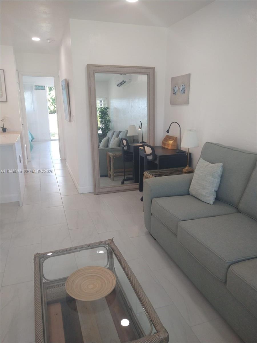 A living room features a light gray sofa, a glass coffee table, and a large mirror — 600 Layne Blvd # 122, Hallandale Beach FL 33009, HALLANDALE BEACH, FL