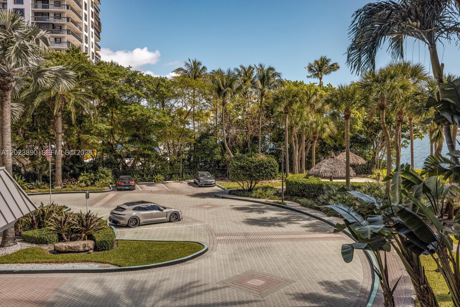 An outdoor view of a paved driveway, parked cars, lush tropical landscaping, and a waterfront building — 2451 Brickell Ave # 2E, Miami FL 33129, MIAMI, FL