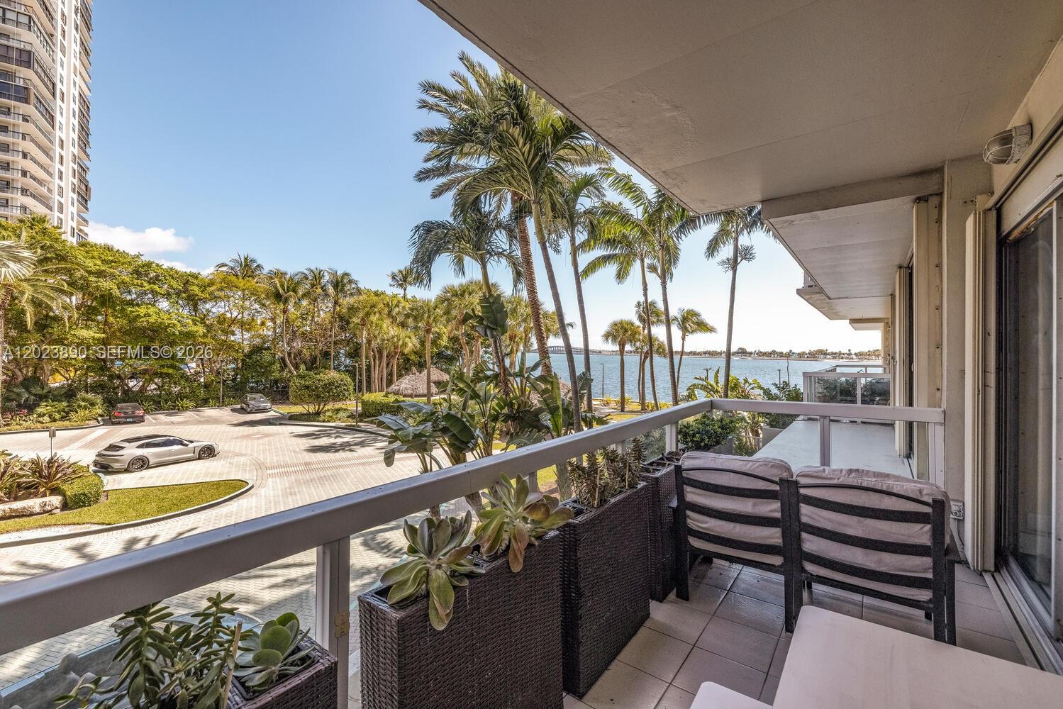 A balcony with potted plants and seating overlooks a parking lot, palm trees, and water — 2451 Brickell Ave # 2E, Miami FL 33129, MIAMI, FL