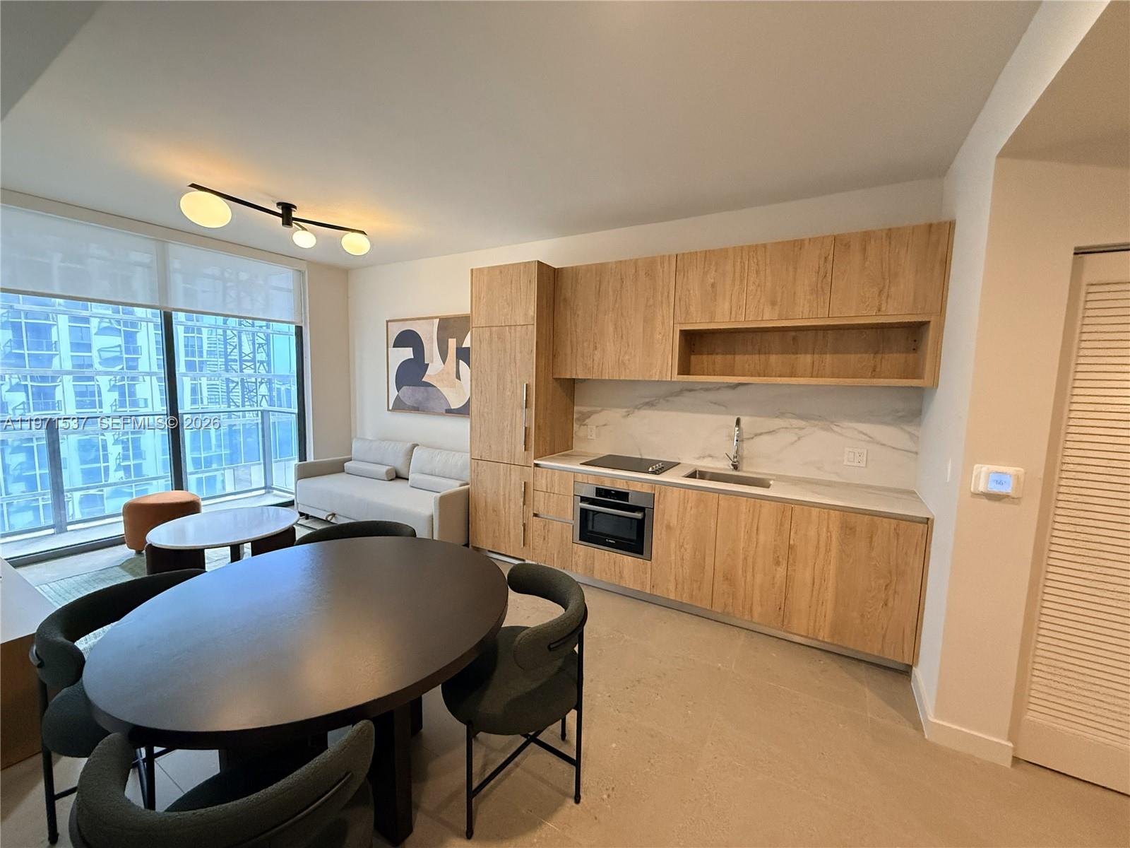 A modern studio apartment features a kitchenette with wood cabinets and a dining area — 11 NE 6th # 1905, Miami FL 33132, MIAMI, FL