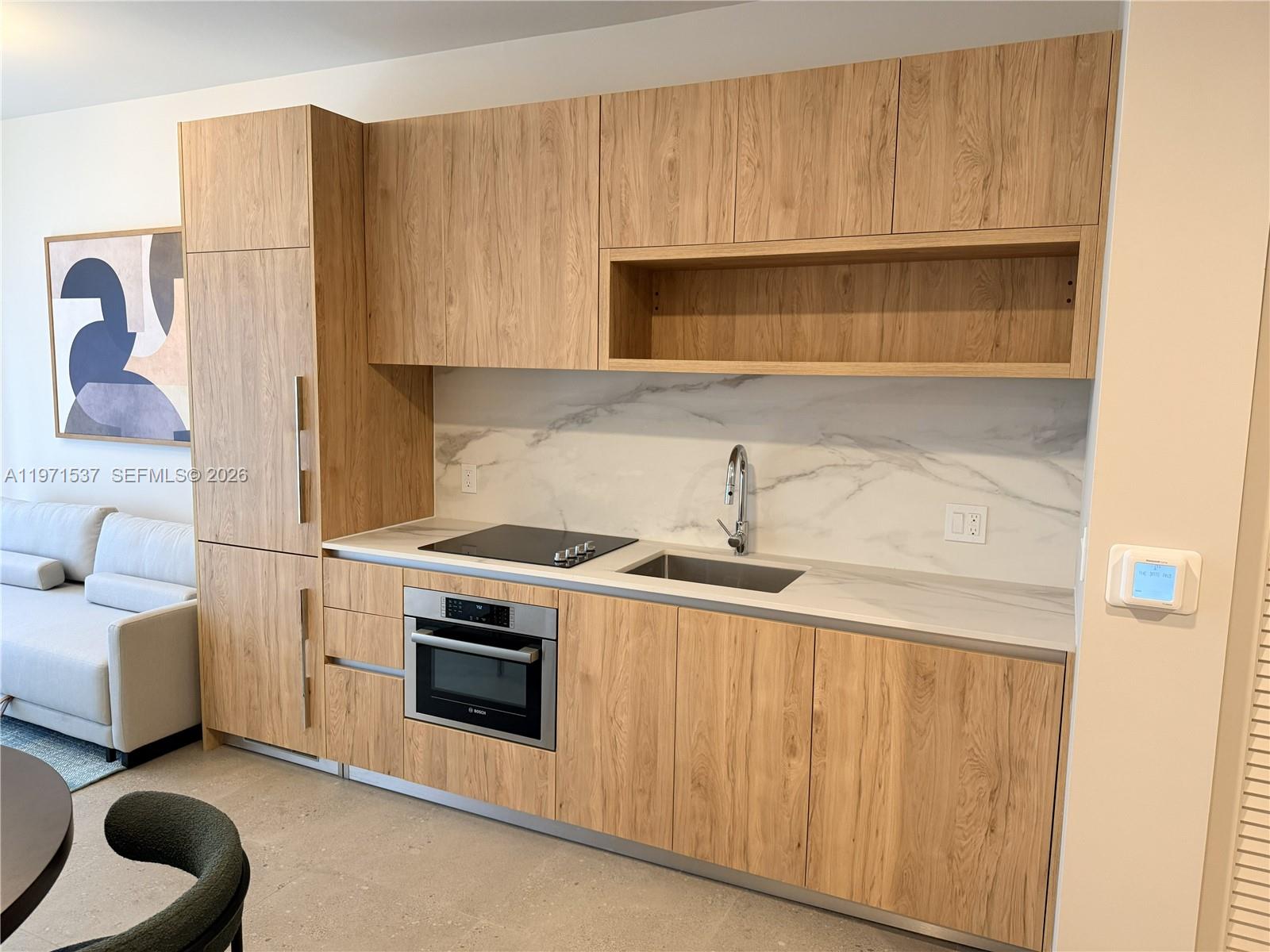 A modern kitchenette features light wood cabinetry, a marble backsplash, and integrated stainless steel appliances — 11 NE 6th # 1905, Miami FL 33132, MIAMI, FL