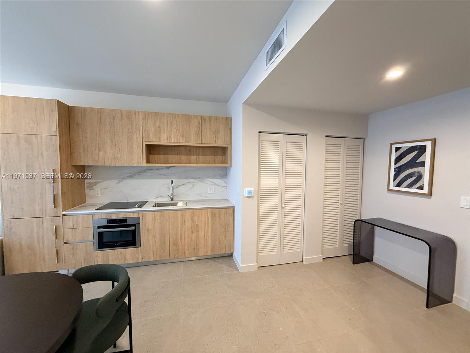 A modern kitchen features light wood cabinetry, marble-look backsplash, and a sleek console table — 11 NE 6th # 1905, Miami FL 33132, MIAMI, FL