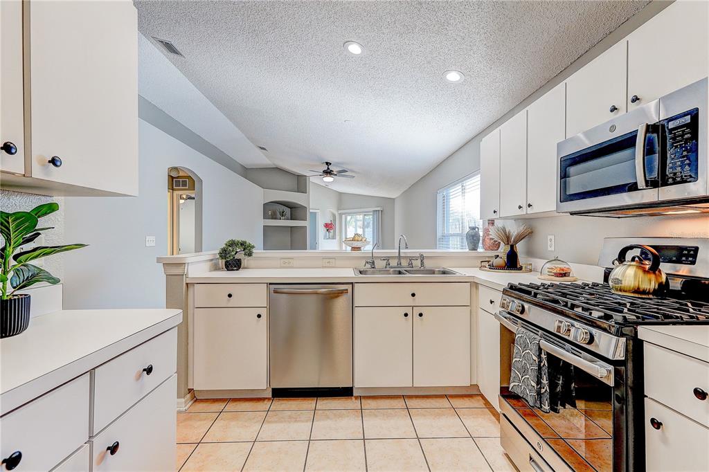 A kitchen features white cabinets, stainless steel appliances, a double sink, and tiled flooring — 28725 SEASHELL COURT, WESLEY CHAPEL, FL