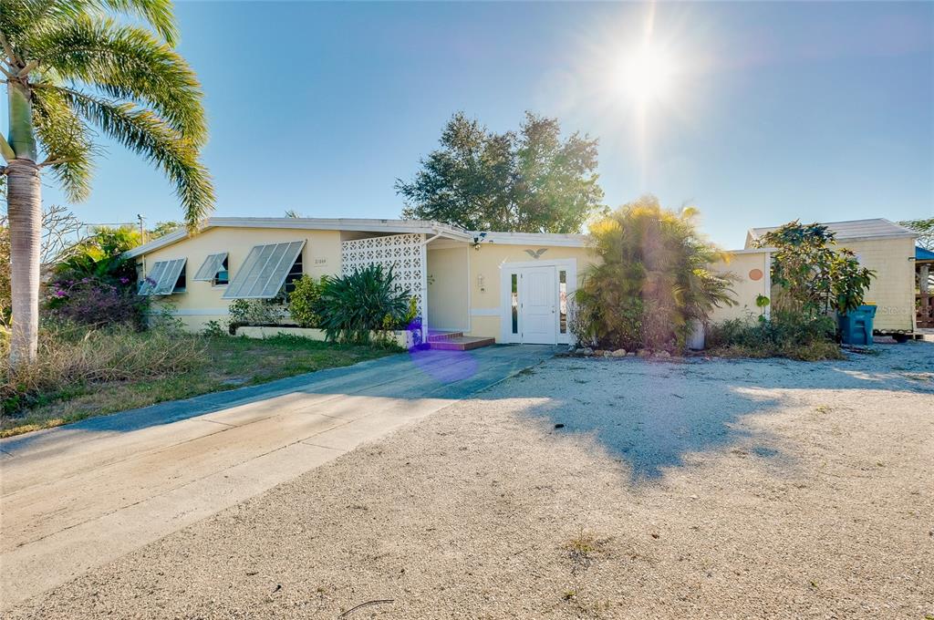 A single-story yellow house with a gravel driveway and a palm tree in the yard — 21064 HIGGS DRIVE, PORT CHARLOTTE, FL