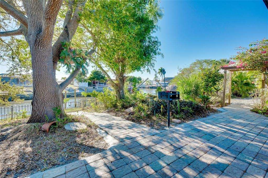 A paved patio area features a charcoal grill, mature trees, and a view of a canal — 21064 HIGGS DRIVE, PORT CHARLOTTE, FL