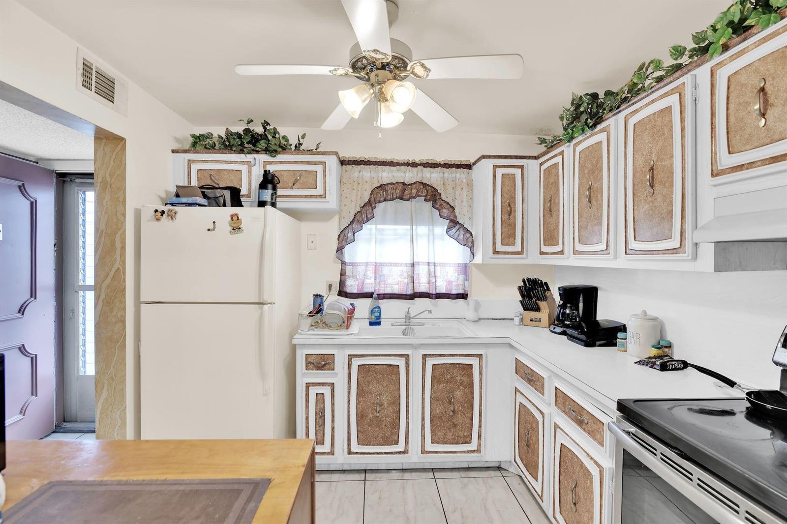 A kitchen features white cabinets with textured brown panels, a white refrigerator, and a ceiling fan — 711 Lori Drive # 204, Palm Springs FL 33461, PALM SPRINGS, FL