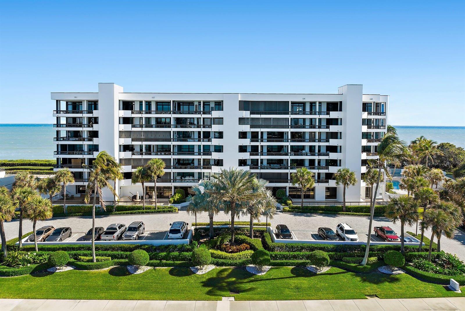 An exterior view of a multi-story white apartment building with palm trees and parking — 19750 S Beach Road # 6050, Jupiter FL 33469, JUPITER, FL