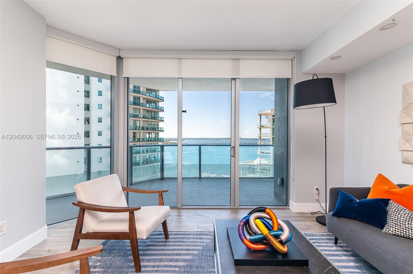 A living room features a balcony with water views, a modern chair, and a sofa — 1300 Brickell Bay Dr # 2509, Miami FL 33131, MIAMI, FL