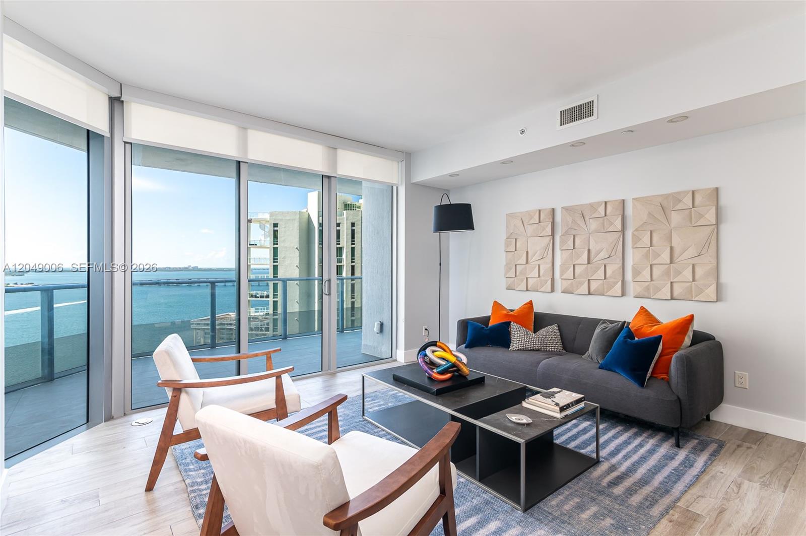 A living room features a gray sofa, two white armchairs, and a balcony with water views — 1300 Brickell Bay Dr # 2509, Miami FL 33131, MIAMI, FL