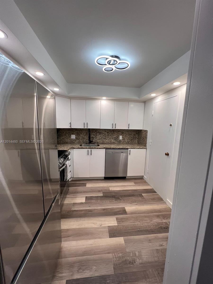 A kitchen features white cabinets, stainless steel appliances, granite countertops, and wood-look flooring — 3800 S Ocean Dr # 1808, Hollywood FL 33019, HOLLYWOOD, FL
