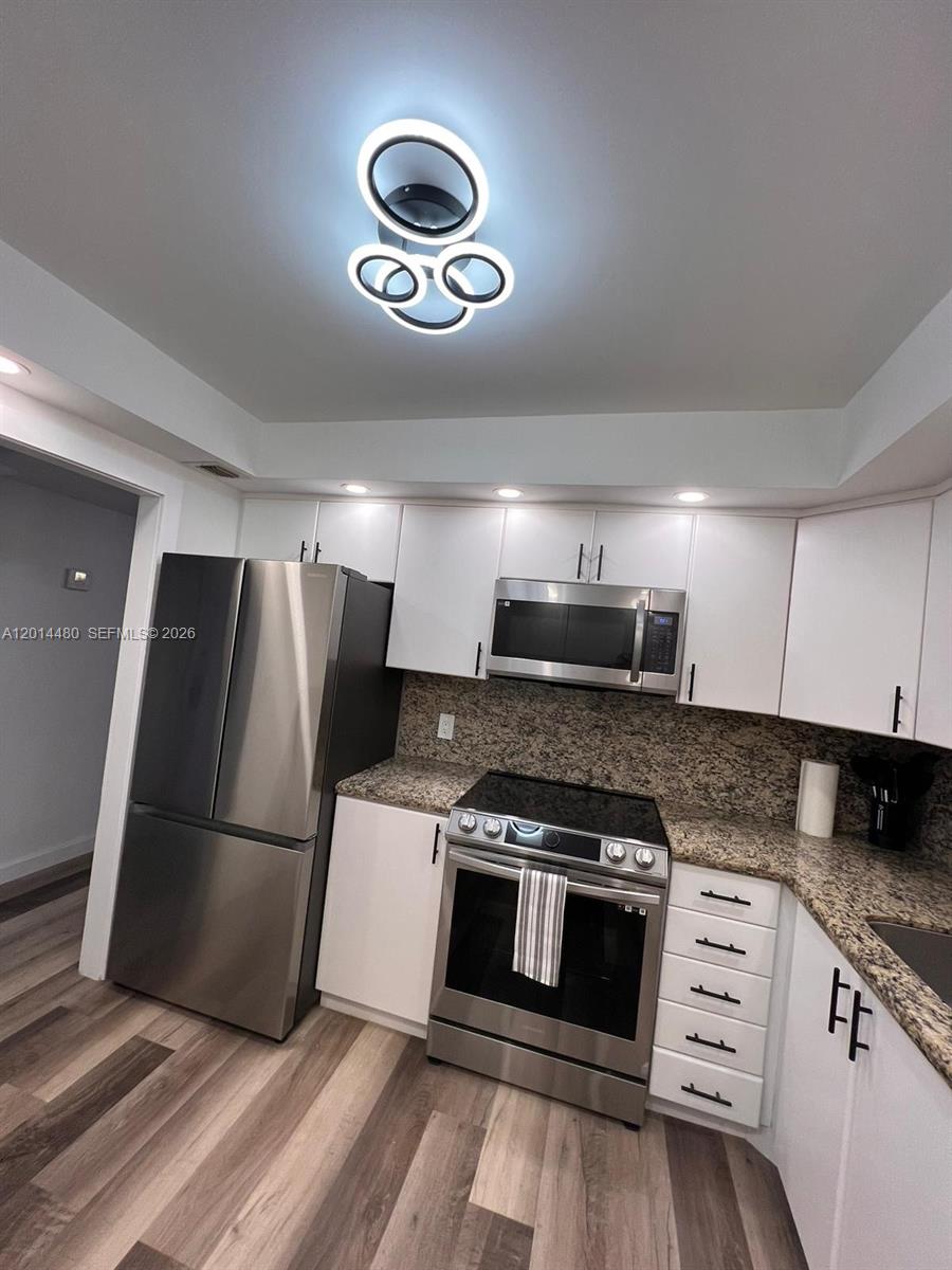 A kitchen features white cabinets, granite countertops, stainless steel appliances, and wood-look flooring — 3800 S Ocean Dr # 1808, Hollywood FL 33019, HOLLYWOOD, FL