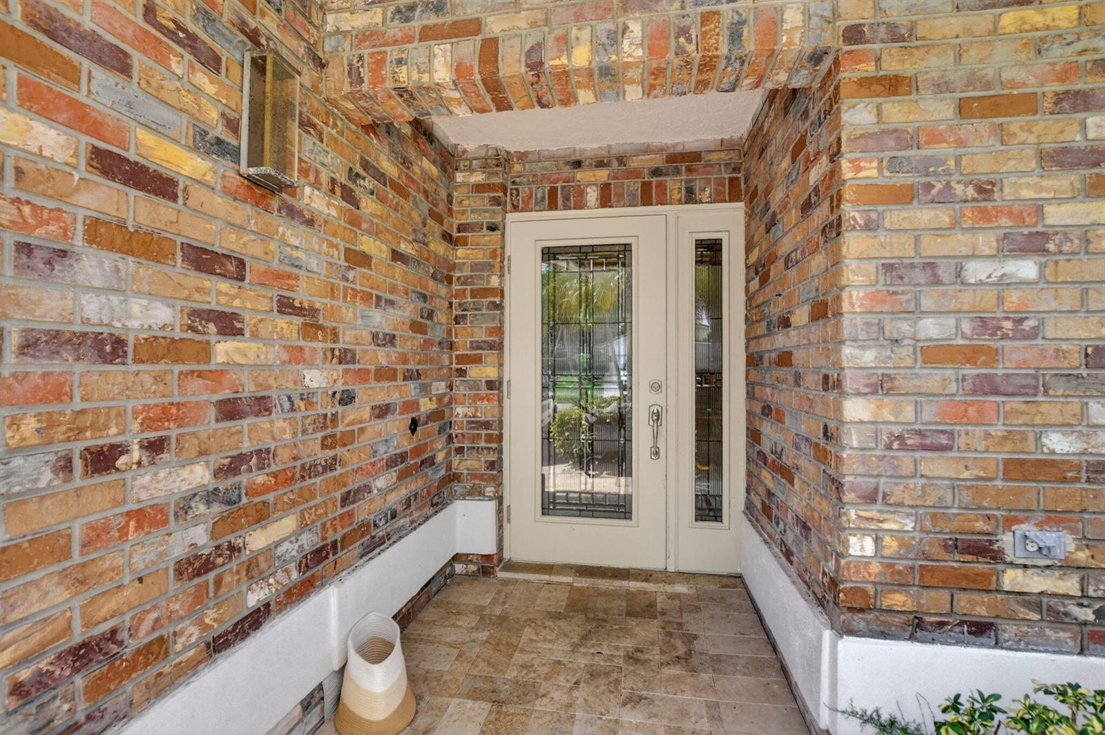 A front entryway with a glass-paneled door, brick walls, and tiled flooring — 10065 Camelback Lane, Boca Raton FL 33498, BOCA RATON, FL