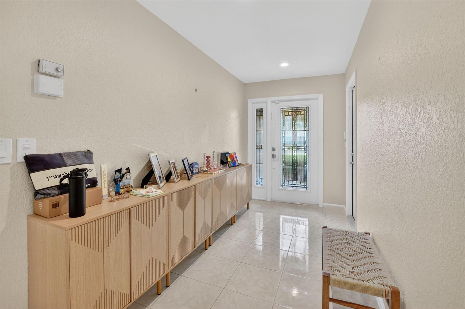 A bright entryway features light-colored tile flooring, a long wooden console table, and a glass-paneled door — 10065 Camelback Lane, Boca Raton FL 33498, BOCA RATON, FL