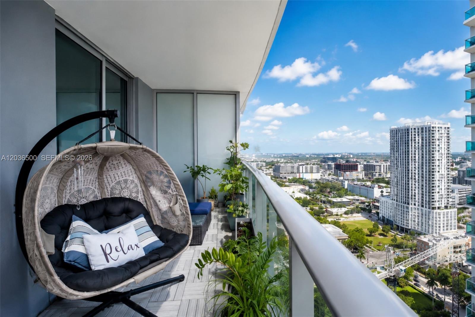 A balcony features a hanging egg chair, potted plants, and a view of city buildings — 488 NE 18th St # 3007, Miami FL 33132, MIAMI, FL