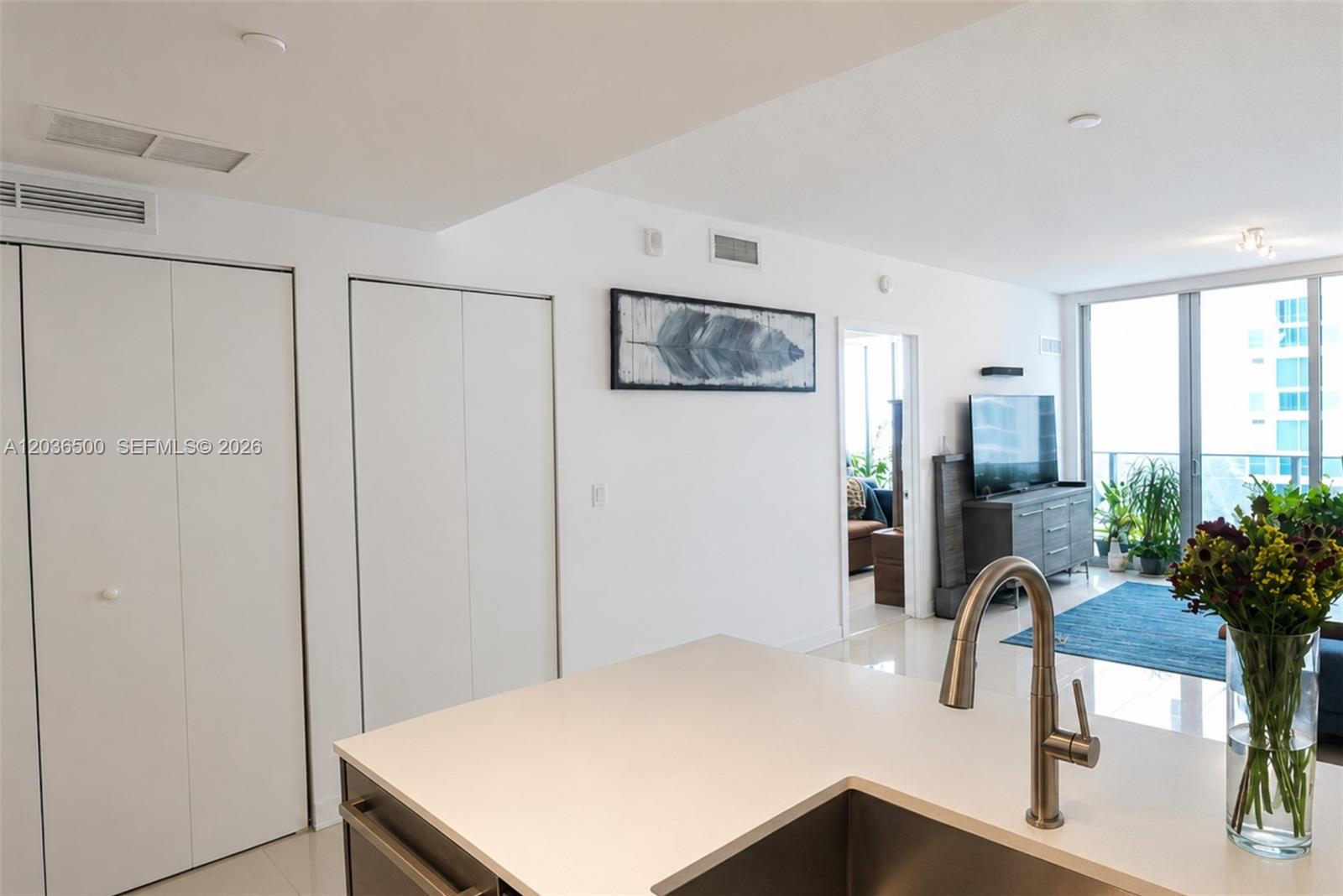 A modern kitchen island with a stainless steel faucet overlooks a bright, open-concept living area — 488 NE 18th St # 3007, Miami FL 33132, MIAMI, FL