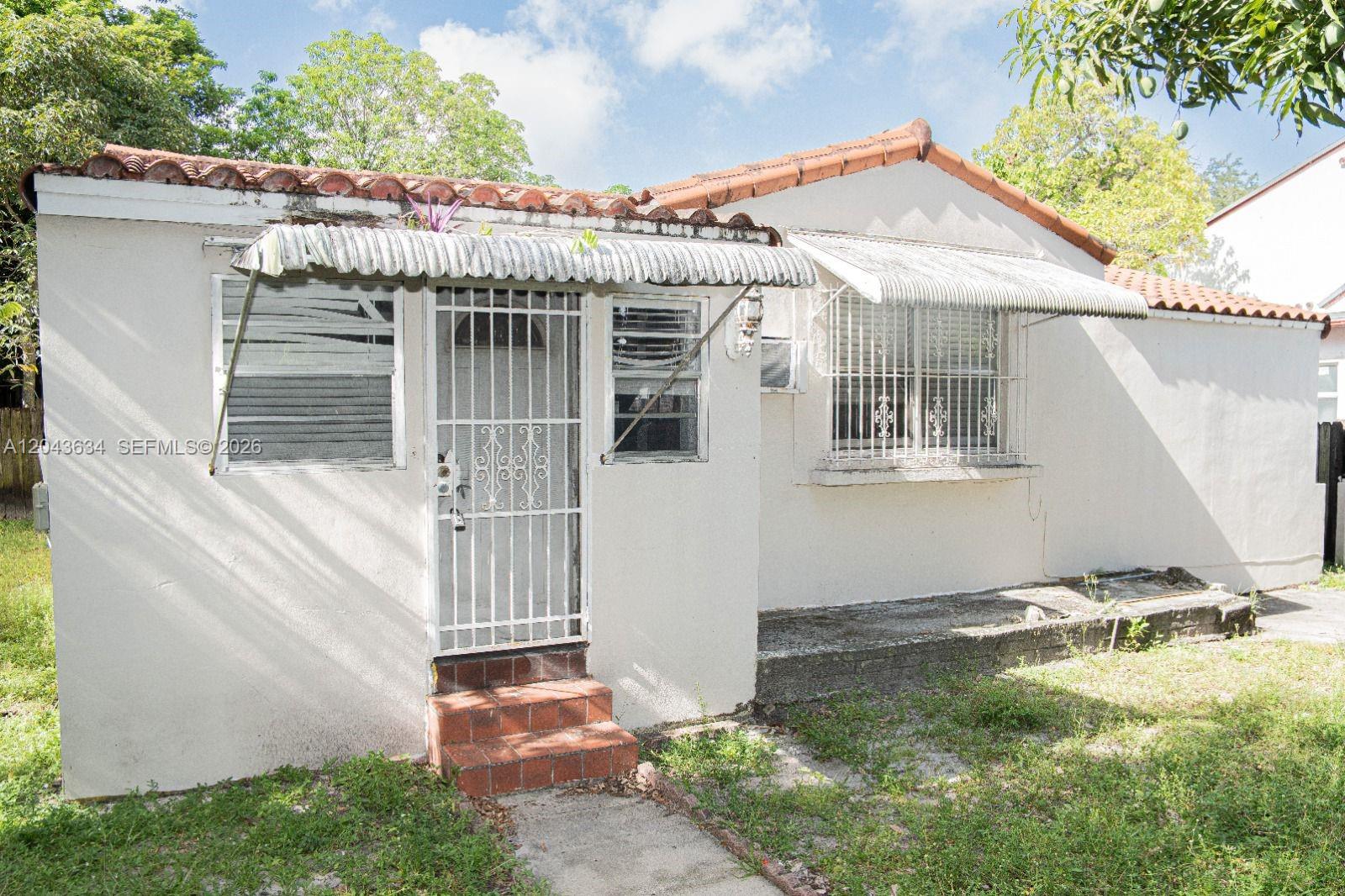 A small, single-story house features a white stucco exterior, terracotta roof tiles, and metal awnings — 90 NE 48th St, Miami FL 33137, MIAMI, FL