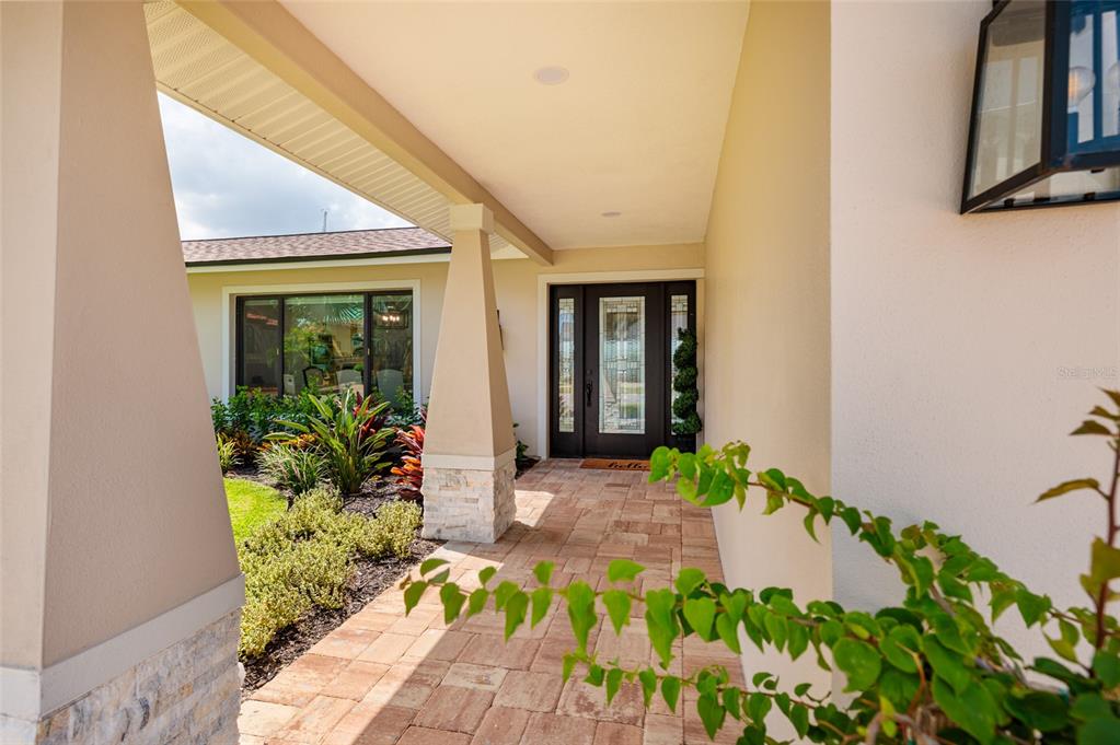 A covered entryway features a stone-based pillar, paver walkway, and a dark-framed glass front door — 825 116TH AVENUE, TREASURE ISLAND, FL