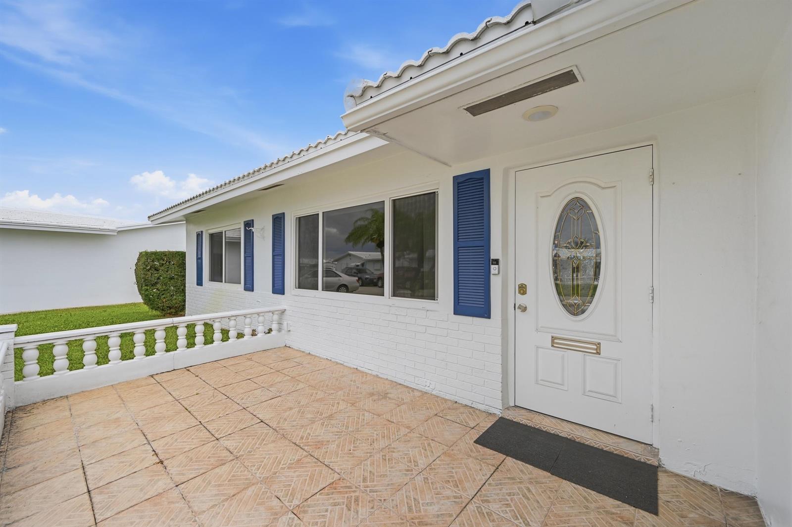 A white brick house exterior features a tiled porch, blue shutters, and a front door — 1316 SW 23rd Street, Boynton Beach FL 33426, BOYNTON BEACH, FL