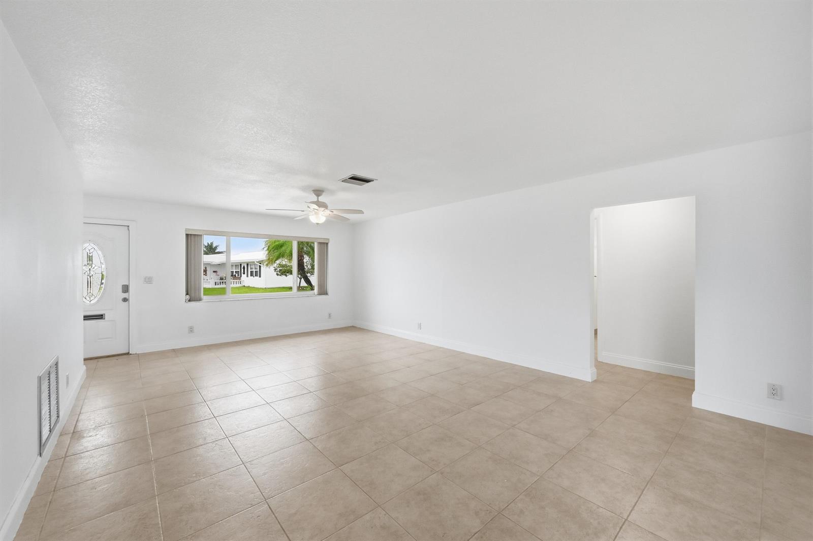 An empty living room features white walls, beige tile flooring, a ceiling fan, and a window — 1316 SW 23rd Street, Boynton Beach FL 33426, BOYNTON BEACH, FL