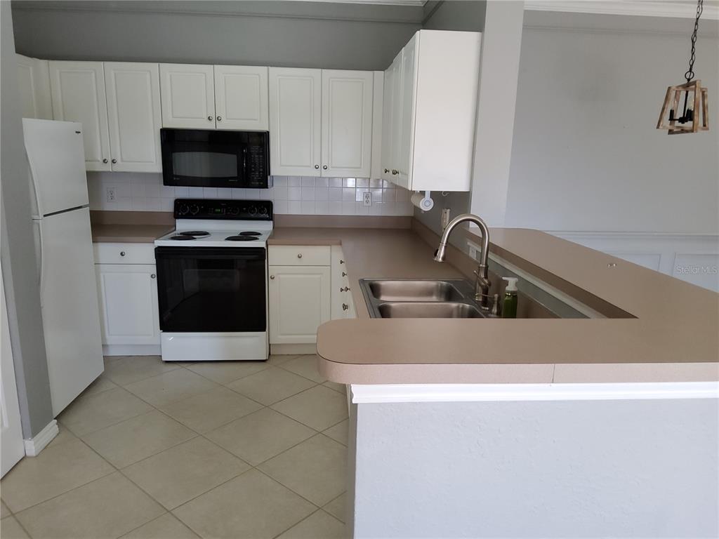 A kitchen features white cabinets, a black stove, a double sink, and tan countertops — 4333 BAYSIDE VILLAGE DRIVE UNIT 224, TAMPA, FL