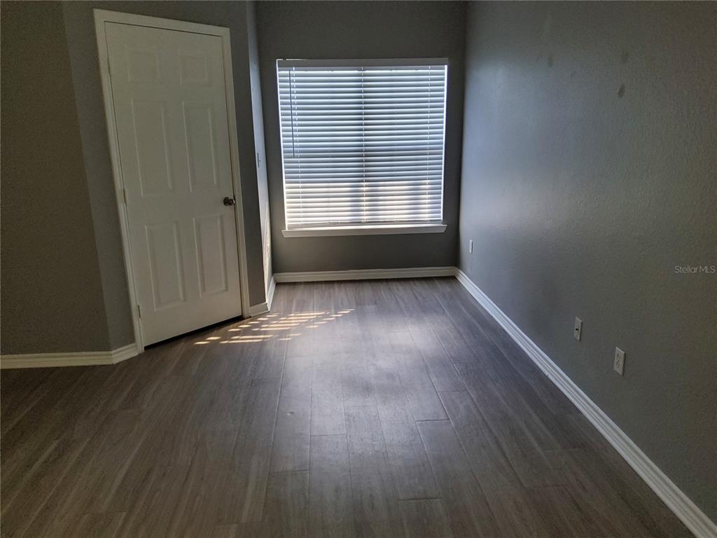 An empty room features gray walls, wood-look flooring, a white door, and a window with blinds — 4333 BAYSIDE VILLAGE DRIVE UNIT 224, TAMPA, FL