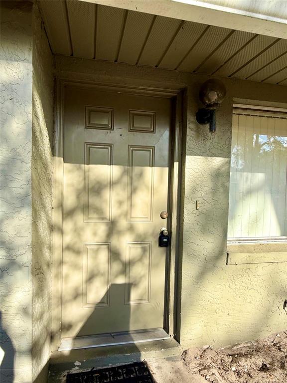A tan exterior door with a lockbox sits under a covered entryway next to a window — 4562 PHEASANT RUN DRIVE UNIT 9B, ORLANDO, FL