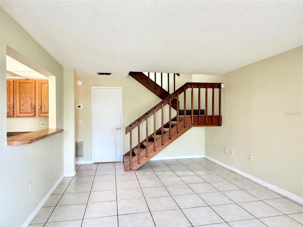 An interior view shows a room with tiled floors, a wooden staircase, and a kitchen pass-through — 4562 PHEASANT RUN DRIVE UNIT 9B, ORLANDO, FL
