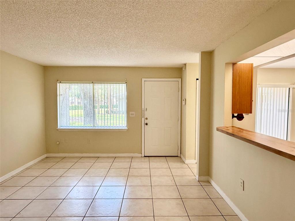 An interior view of a room with beige walls, tiled flooring, a window, and a door — 4562 PHEASANT RUN DRIVE UNIT 9B, ORLANDO, FL